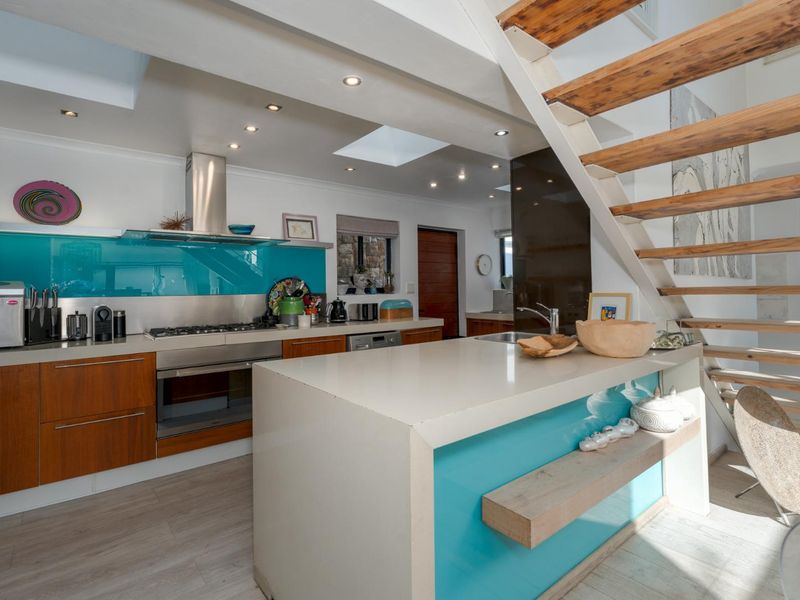 Modern kitchen featuring a central island, stone countertops, integrated appliances, and a striking staircase, illuminated by natural light from overhead skylights.