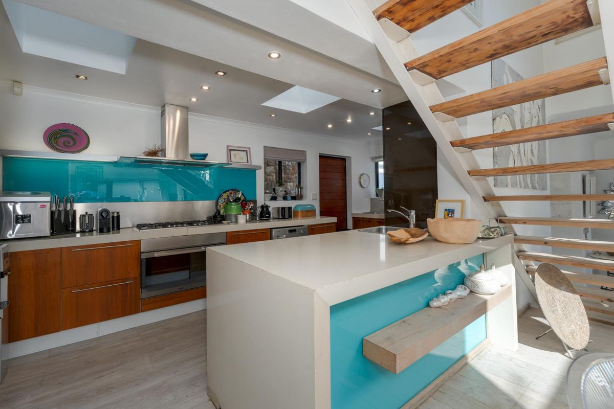 Modern kitchen featuring a central island, stone countertops, integrated appliances, and a striking staircase, illuminated by natural light from overhead skylights.
