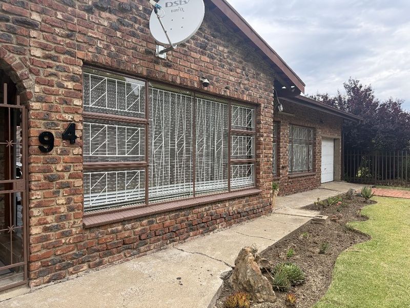 Front exterior view of a face brick house featuring security bars on windows, a concrete walkway, and an attached garage.