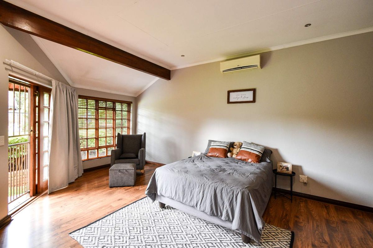 A spacious bedroom featuring vaulted ceilings with exposed timber beams, wood-look flooring, and direct access to an outdoor area through glass-paned doors.