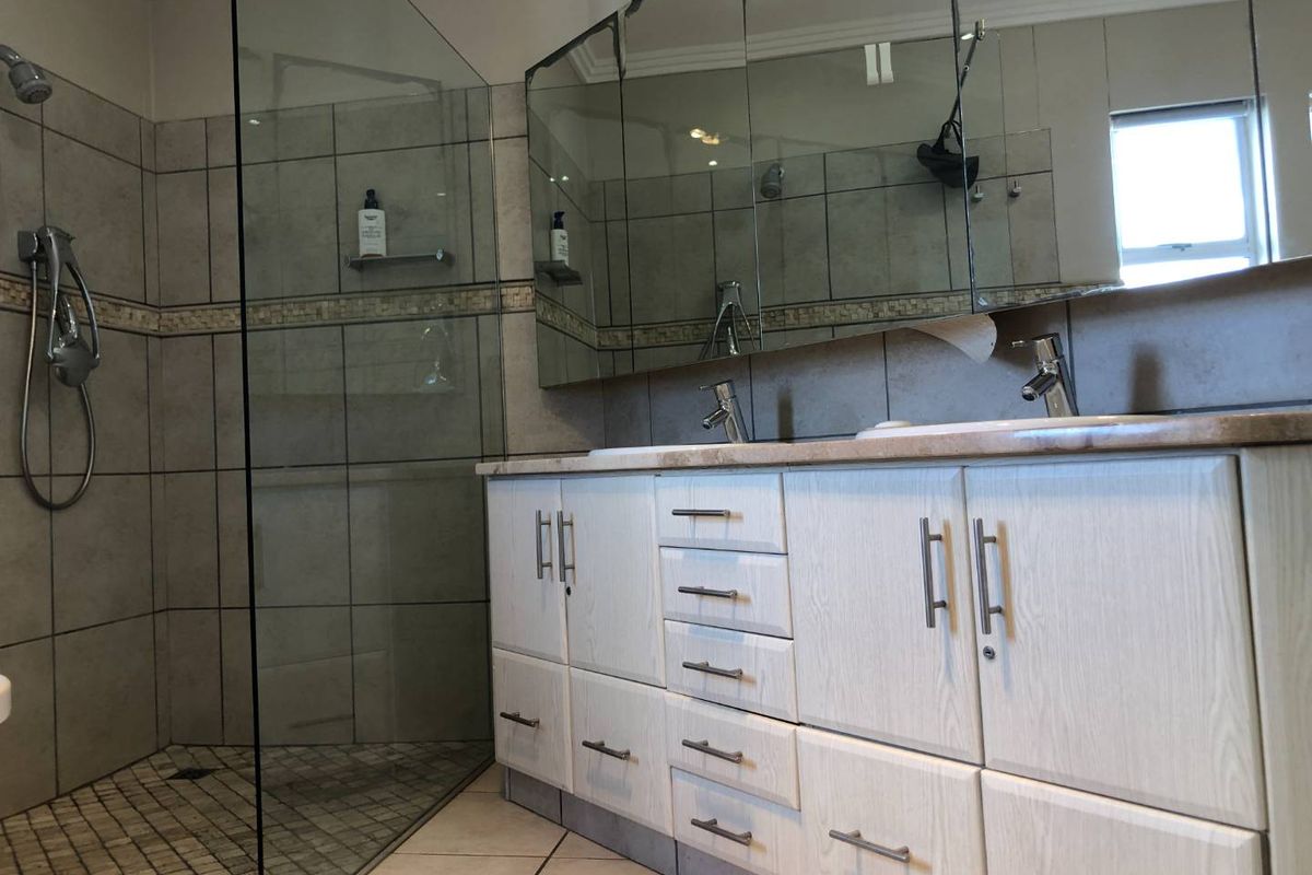 Modern bathroom featuring a double vanity with stone countertop, large wall-mounted mirror cabinets, and a spacious walk-in glass shower enclosure.