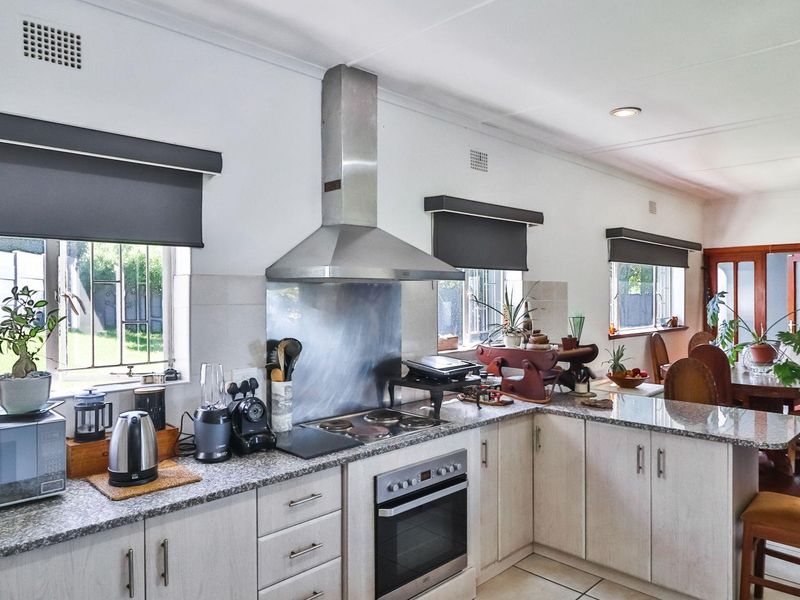 Open-plan kitchen featuring granite countertops, built-in oven, electric hob, and stainless steel extractor fan, seamlessly flowing into the dining area.