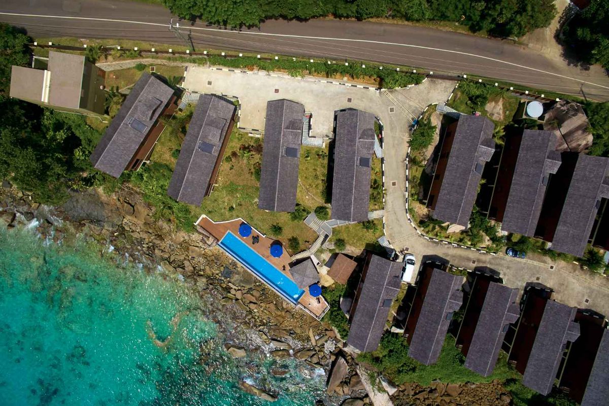 Aerial view of a coastal commercial property complex featuring multiple detached units, a swimming pool, and direct oceanfront access.
