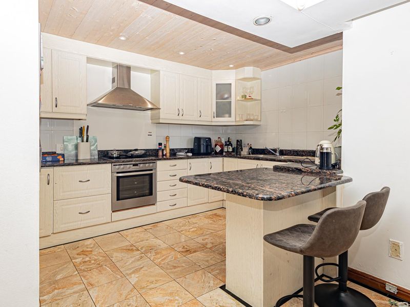 A functional kitchen featuring light-toned cabinetry, granite countertops, a breakfast bar, and stainless steel appliances, complemented by tiled flooring and recessed lighting.