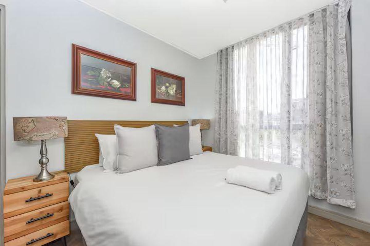 A well-maintained bedroom featuring herringbone timber flooring, a modern timber-look headboard, and floor-to-ceiling sheer curtains allowing for natural light.