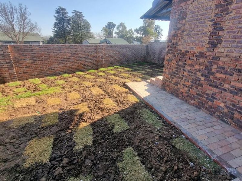 Rear exterior view of the property featuring a face brick facade, paved walkway, and a garden area currently undergoing landscaping.
