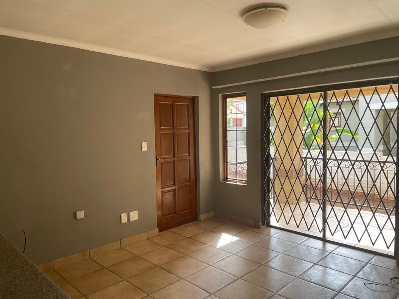 An empty living area featuring tiled floors, a wooden door, and a sliding glass door with a security gate leading to an outdoor space.