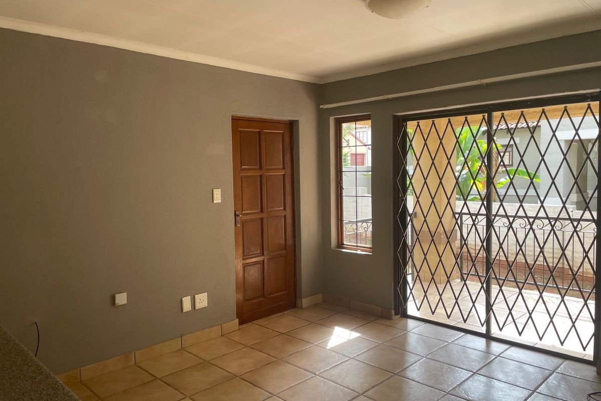 An empty living area featuring tiled floors, a wooden door, and a sliding glass door with a security gate leading to an outdoor space.