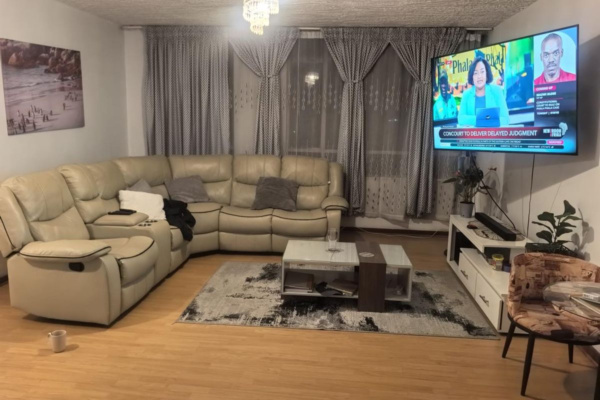 A comfortable living room featuring laminate flooring and large window treatments, providing a functional and inviting space for relaxation.