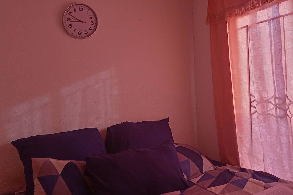 A bedroom featuring a window with security bars and a wall-mounted clock, providing a functional sleeping space.