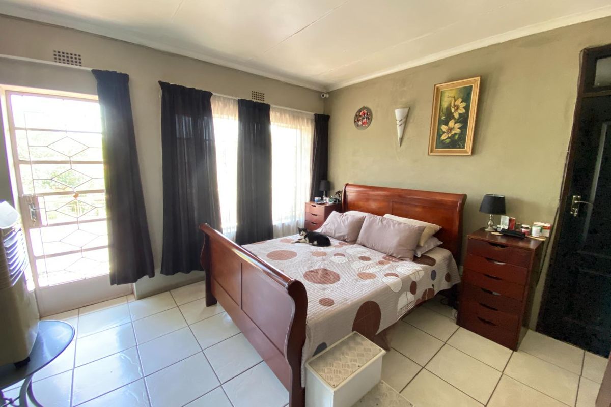 A bedroom featuring tiled flooring, large windows with security bars, and a glass-panelled exterior door providing natural light.