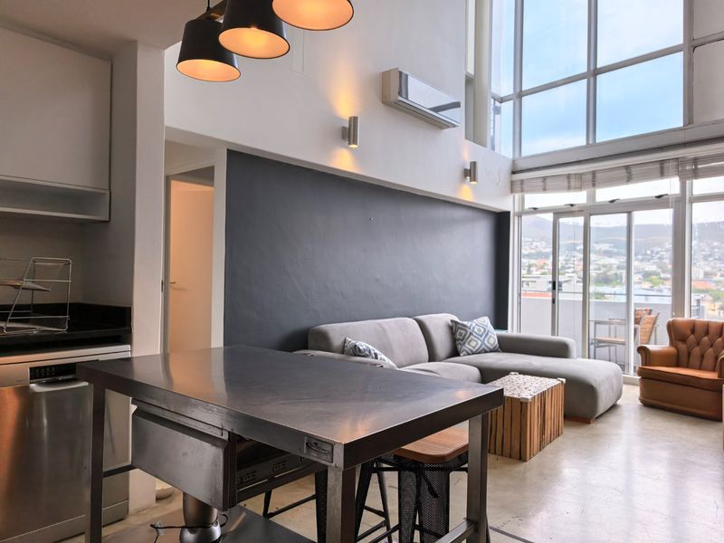 Modern open-plan living area featuring double-volume windows, high ceilings, a sleek kitchen island, and direct access to a balcony with urban views.