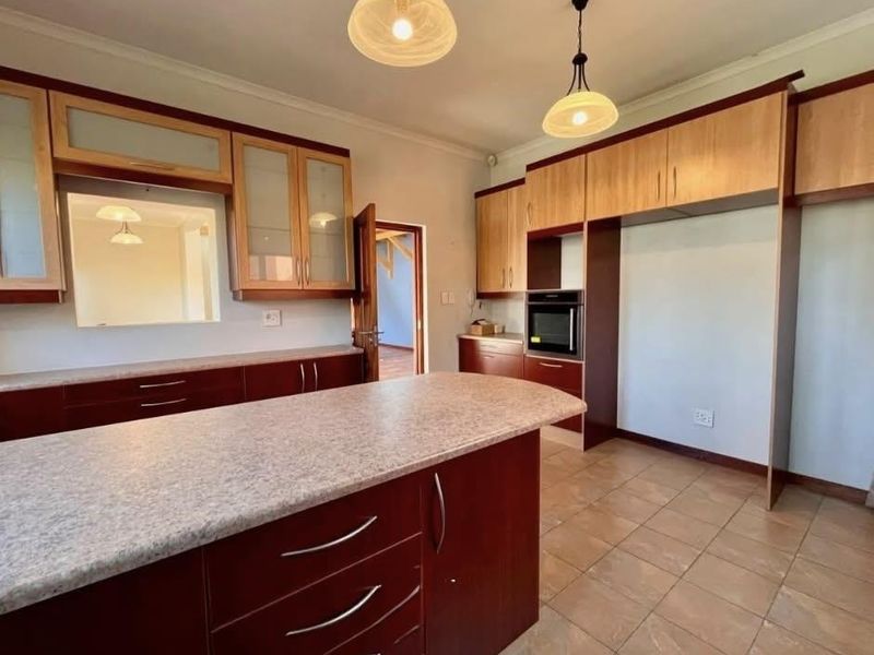 A spacious kitchen featuring two-tone built-in cabinetry, a central island with laminate countertops, a built-in oven, and tiled flooring.