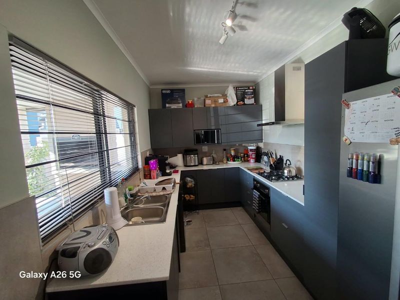 Modern kitchen featuring dark grey cabinetry, stone countertops, integrated appliances including a gas hob, oven, and extractor fan, with tiled flooring.