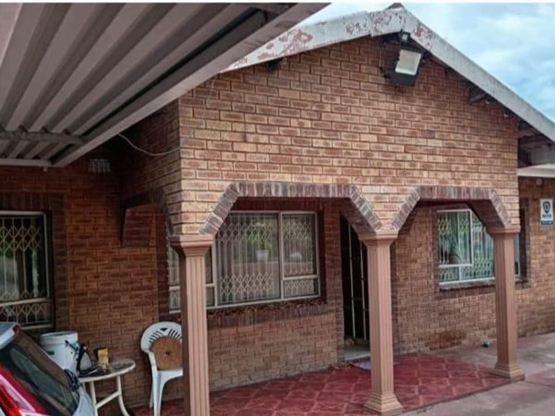 Front elevation of a face brick house featuring a covered patio with decorative columns, security bars on windows, and an attached carport.