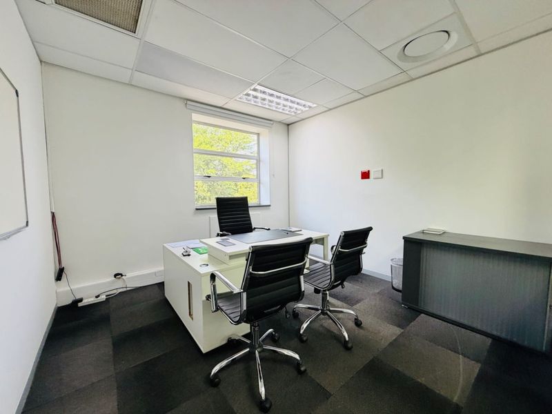 A functional office space featuring a suspended ceiling with recessed lighting, carpet tile flooring, and a window providing natural light.