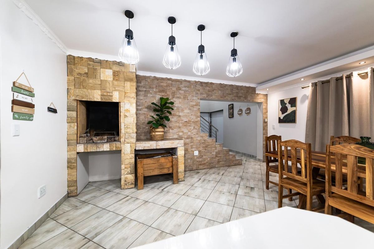 Spacious living area featuring a prominent stone-clad indoor braai, tiled flooring, and modern pendant lighting, creating a warm and inviting atmosphere.