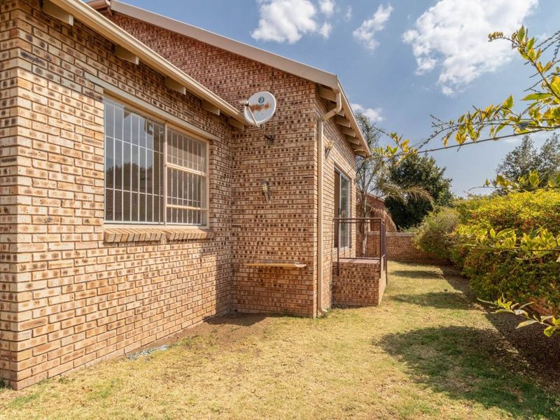 Rear view of the townhouse featuring a face brick facade, security bars on windows, and a private garden area with boundary walling.