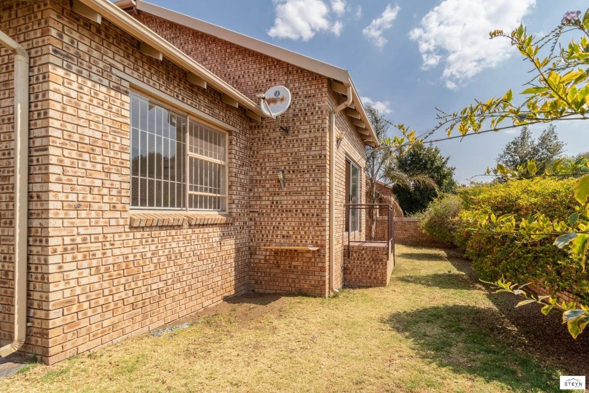 Rear view of the townhouse featuring a face brick facade, security bars on windows, and a private garden area with boundary walling.