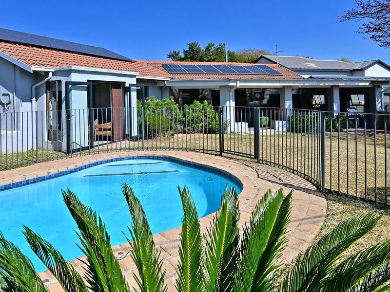 Rear exterior view featuring a swimming pool with paved surround, metal fencing, and a house with a tiled roof and installed solar panels.
