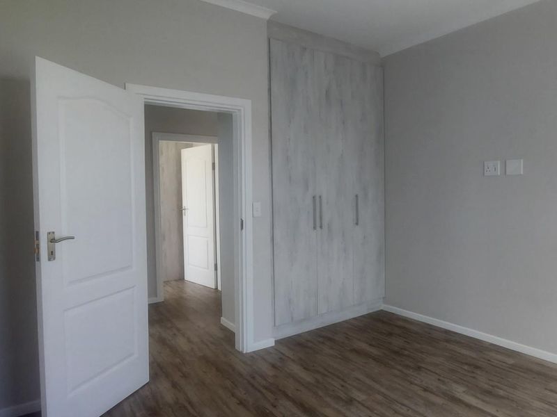 A clean, empty bedroom featuring modern laminate flooring, neutral wall tones, and built-in cupboards, offering a versatile space ready for personalization.