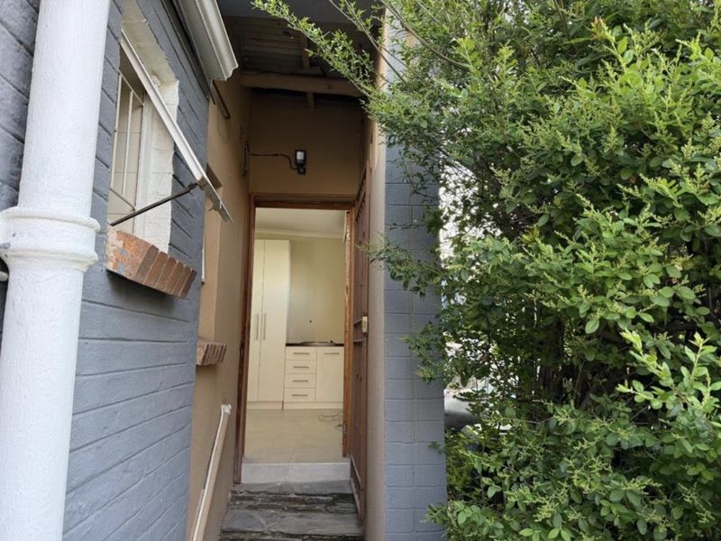 View of the rear exterior entrance showing a stone step, security bars on the window, and a glimpse into the interior kitchen area.