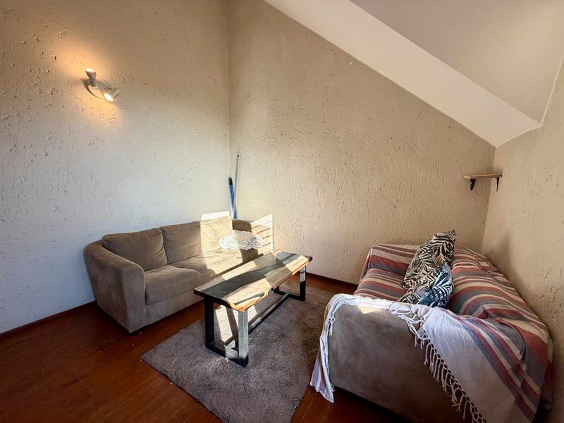 A living room area featuring sloped ceilings, textured walls, and hardwood flooring, providing a cozy space with potential for modern updates.
