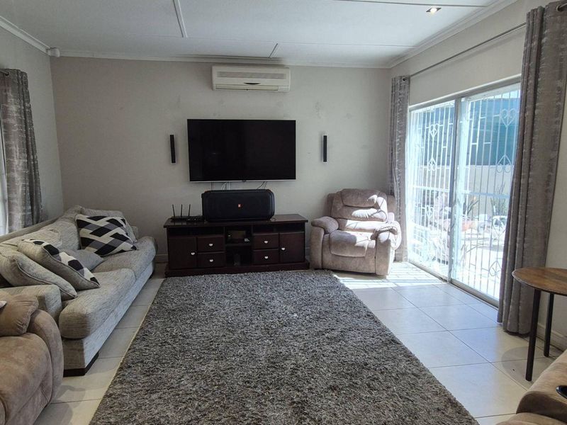 A spacious living room featuring tiled flooring, a wall-mounted air conditioning unit, and dual sliding glass doors with security gates providing natural light.