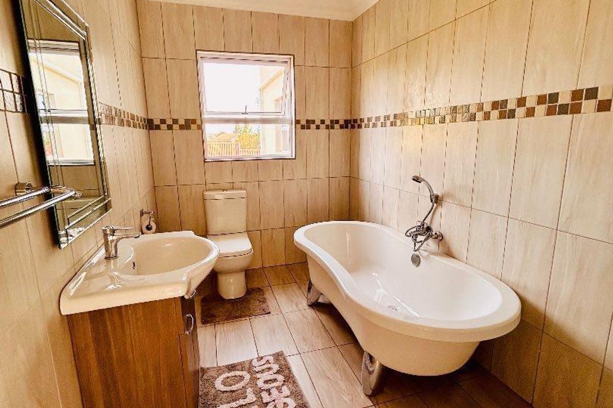 A well-maintained bathroom featuring a freestanding bathtub, a vanity basin with storage, and neutral floor-to-ceiling wall tiling.
