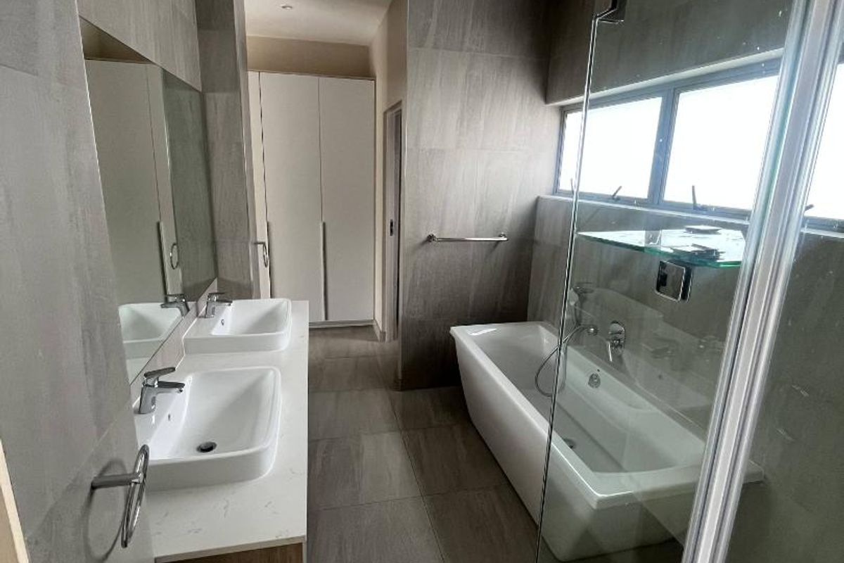 Modern bathroom featuring a double vanity with stone countertop, a freestanding bathtub, a glass-enclosed shower, and floor-to-ceiling neutral tiling.