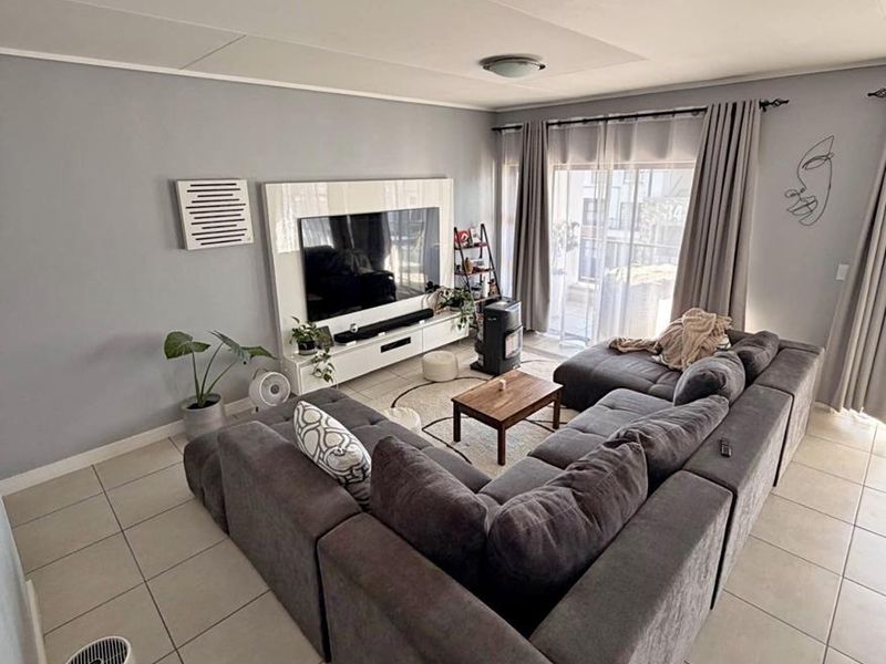 A well-maintained living room featuring neutral grey walls, large format floor tiles, and a sliding glass door providing access to the outdoor area.