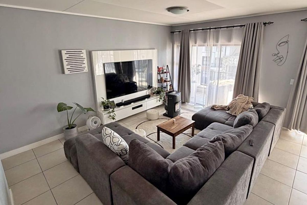 A well-maintained living room featuring neutral grey walls, large format floor tiles, and a sliding glass door providing access to the outdoor area.