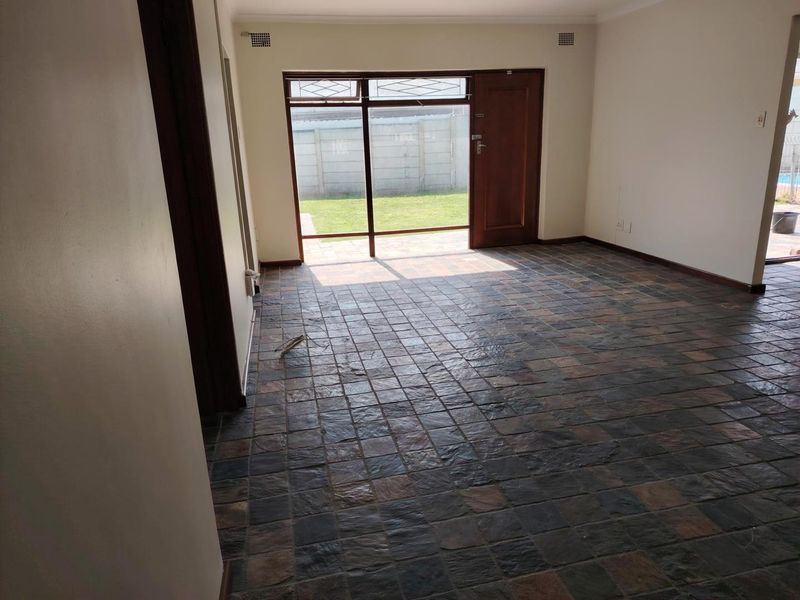 An empty living room featuring dark slate tile flooring and a large glass door providing direct access to the rear garden.