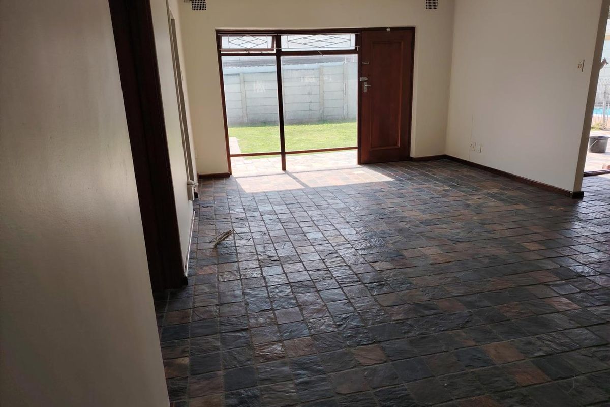 An empty living room featuring dark slate tile flooring and a large glass door providing direct access to the rear garden.