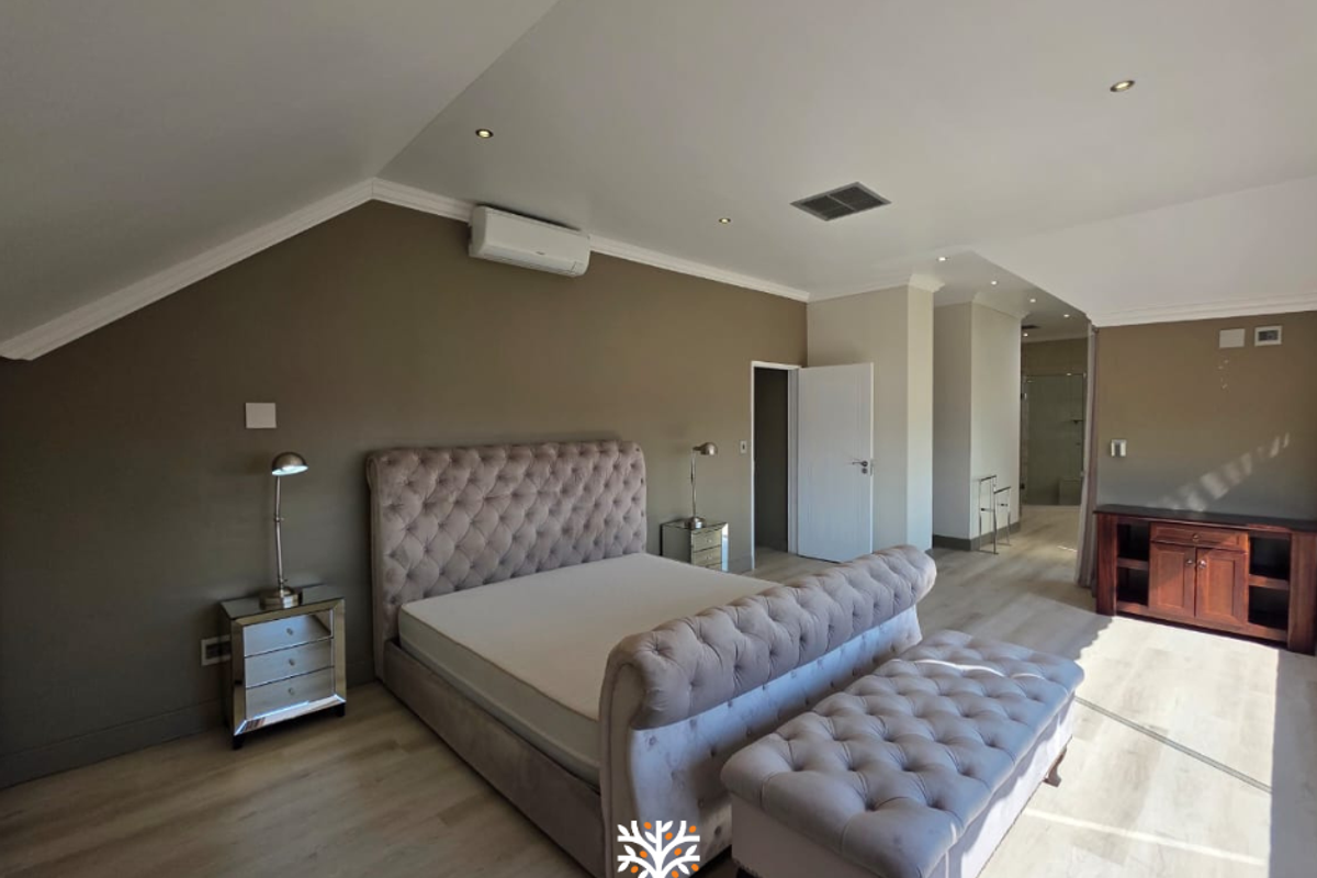 Spacious bedroom featuring laminate flooring, recessed lighting, and a wall-mounted air conditioning unit, with an adjoining en-suite area.