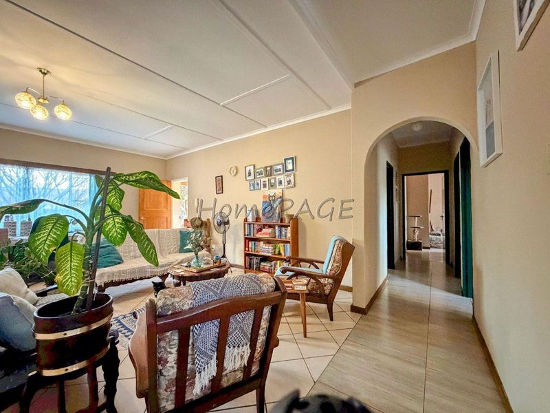 A living room featuring tiled flooring and an arched entryway leading to a hallway, with neutral wall tones and a ceiling light fixture.