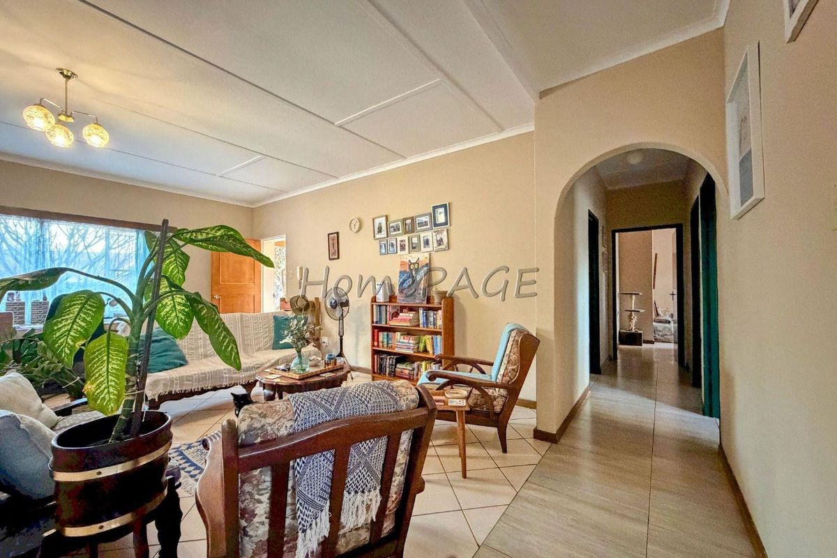 A living room featuring tiled flooring and an arched entryway leading to a hallway, with neutral wall tones and a ceiling light fixture.