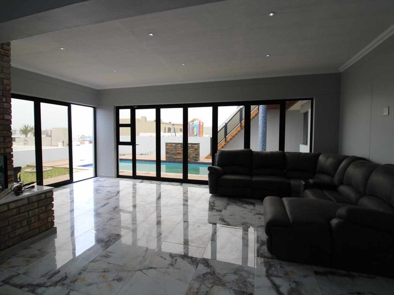 Spacious living room featuring polished marble-look floor tiles, an exposed brick fireplace, and large black aluminium sliding doors opening to the pool area.