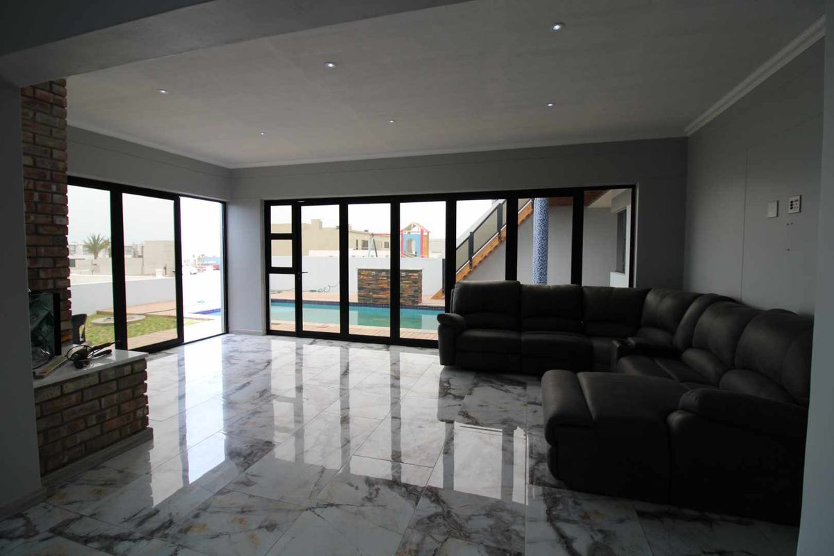 Spacious living room featuring polished marble-look floor tiles, an exposed brick fireplace, and large black aluminium sliding doors opening to the pool area.