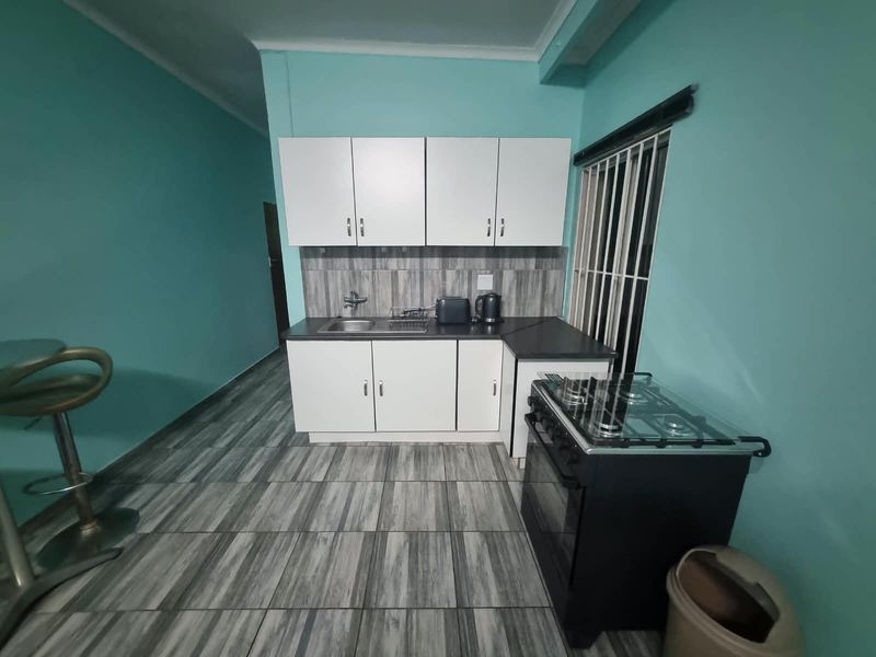 Compact kitchen featuring white cabinetry, dark laminate countertops, a stainless steel sink, and a freestanding gas stove with tiled flooring.