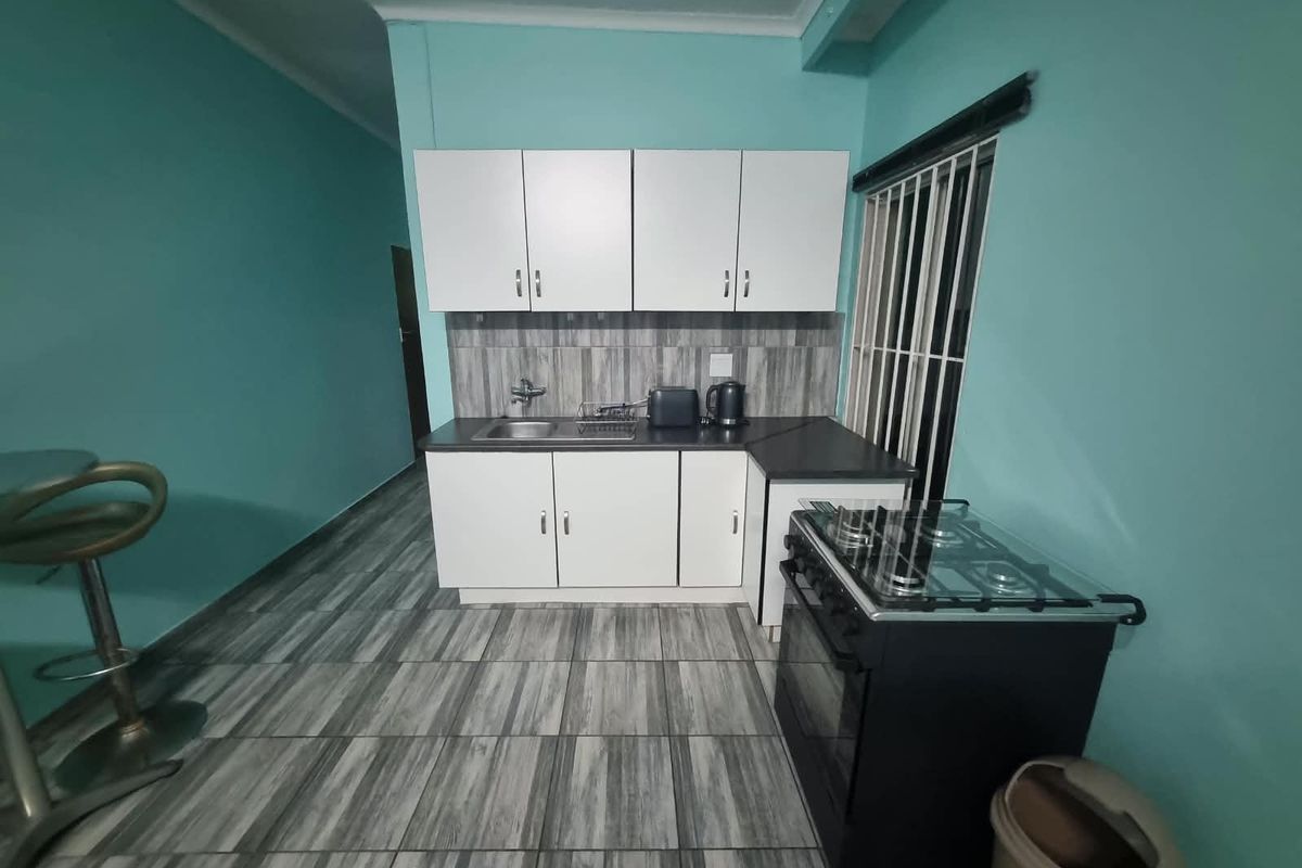 Compact kitchen featuring white cabinetry, dark laminate countertops, a stainless steel sink, and a freestanding gas stove with tiled flooring.