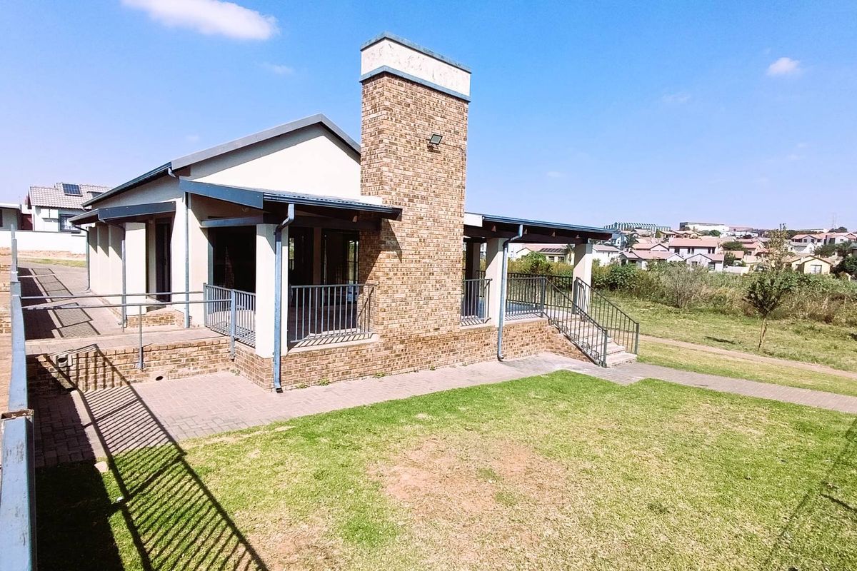 Exterior view of the property featuring a brick chimney, covered patio area with metal railings, and a surrounding lawn.