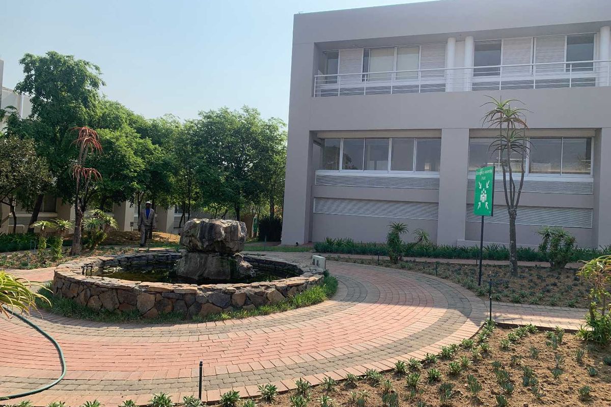 Exterior view of a modern office building featuring a landscaped garden, stone water feature, and paved circular walkway.