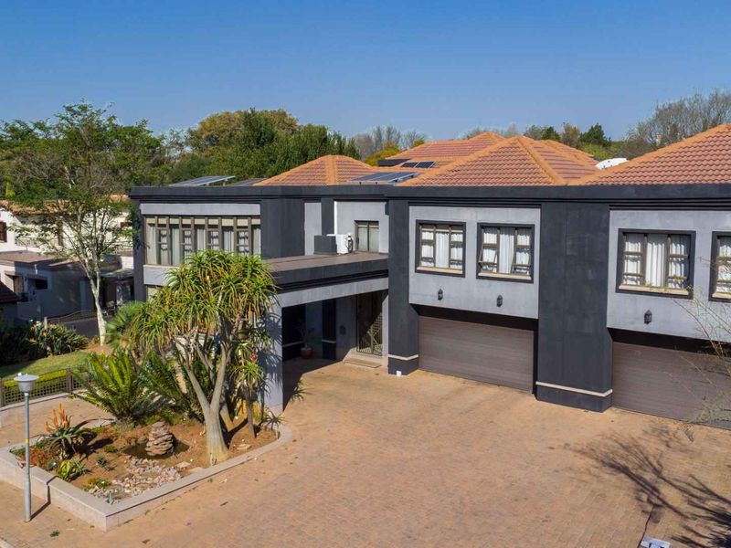 A modern double-story residence featuring a paved driveway, double garage, tiled roof with solar panels, and a well-maintained front garden.