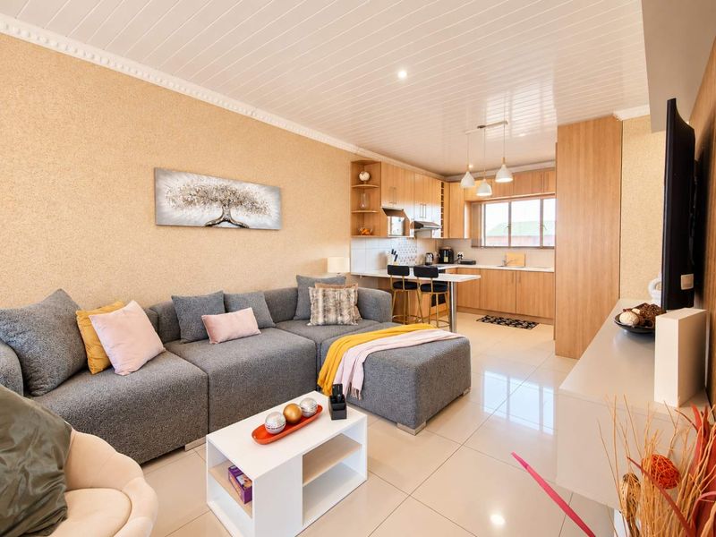 Open-plan living area featuring a modern kitchen with light wood cabinetry, breakfast bar, and tiled flooring throughout, creating a cohesive and functional living space.