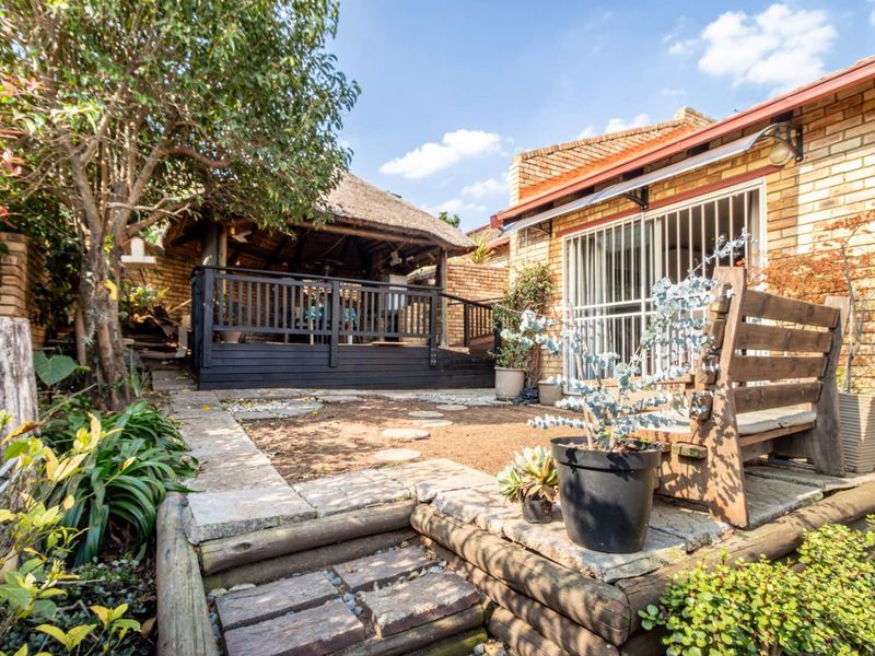 Rear garden area featuring a thatched lapa, timber decking, and brick townhouse facade with security gate access.