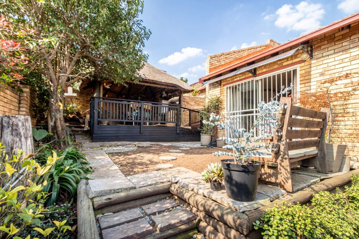 Rear garden area featuring a thatched lapa, timber decking, and brick townhouse facade with security gate access.