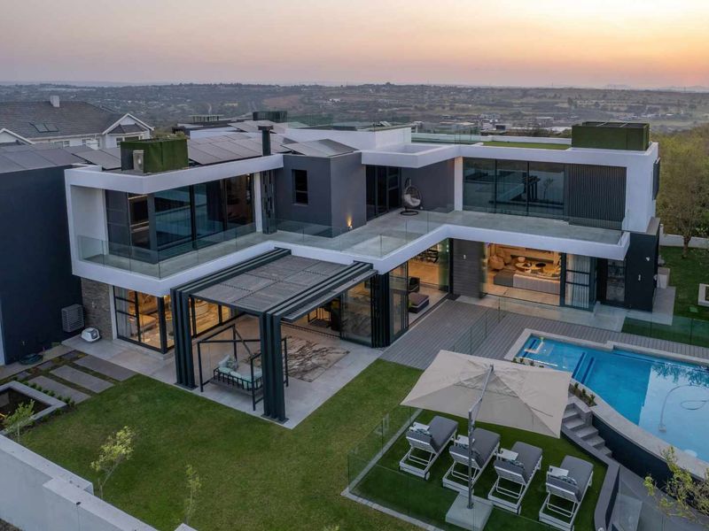 Aerial view of a modern luxury residence featuring a swimming pool, expansive decking, covered patio, and landscaped garden with solar panel installation.