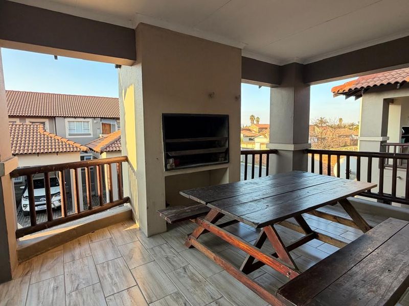 Covered balcony featuring a built-in braai, tiled flooring, and a wooden balustrade, offering an outdoor entertainment space.