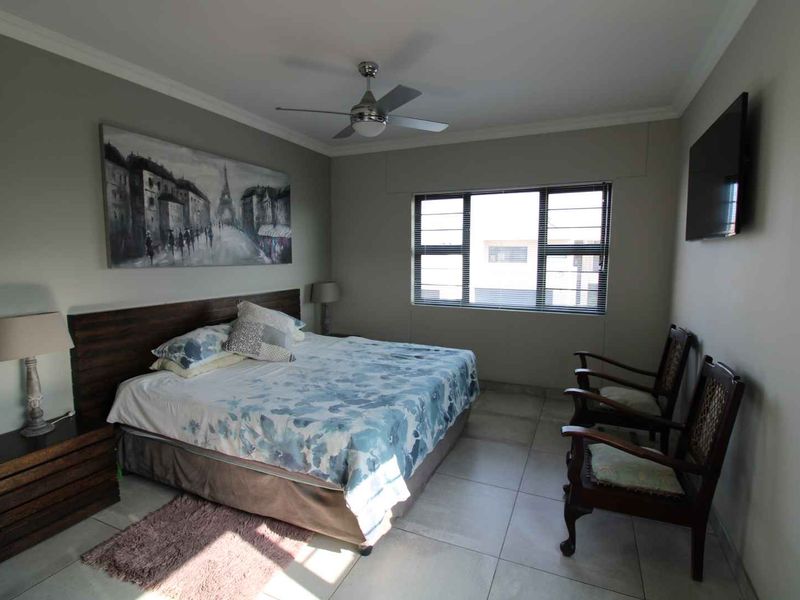 A well-maintained bedroom featuring tiled flooring, a ceiling fan, and a window with security bars, providing a functional and comfortable living space.